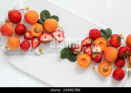 Fruits colorés - fraises et pêches - sur un plateau en marbre sur fond blanc Banque D'Images