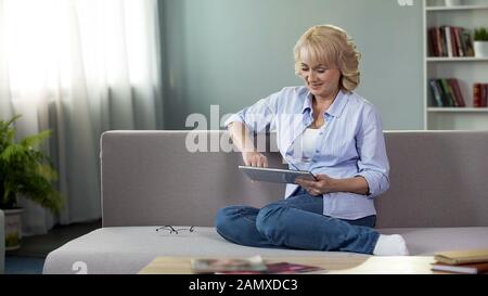 Heureuse femme d'âge moyen regardant des vidéos drôles sur tablette, assis sur le canapé à la maison Banque D'Images