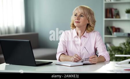 Femme mûre pensant avec bloc-notes sur la table, femme au foyer occupée, planification de la journée Banque D'Images