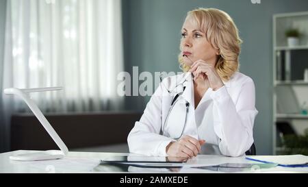 Médecin féminin attentif assis à la table, analyse des résultats du patient, diagnostic Banque D'Images