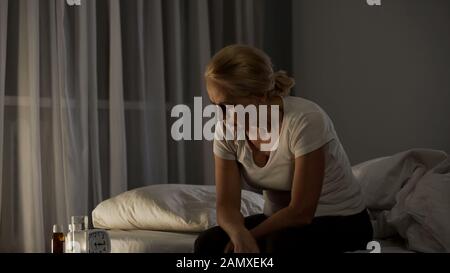 Femme mûre assise sur le lit, souffrant de dépression, pilules sur table, problème Banque D'Images