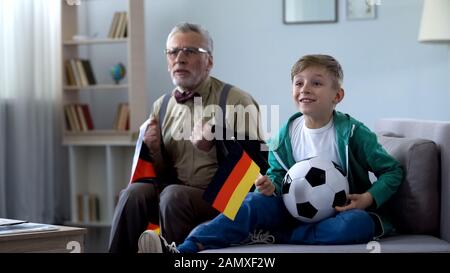 Grand-père enveloppé dans le drapeau allemand regarder le football avec garçon, s'inquiéter du jeu Banque D'Images