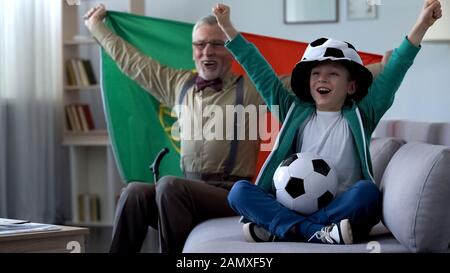 Grand-père tenant le drapeau portugais, célébrant la victoire de l'équipe de football avec garçon Banque D'Images