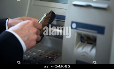 Mains du Mans mettant des dollars dans le portefeuille, l'argent retiré de l'ATM, voyager à l'étranger Banque D'Images