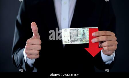 Homme d'affaires tenant des billets roubles russes montrant des pouces vers le haut, flèche tombant Banque D'Images