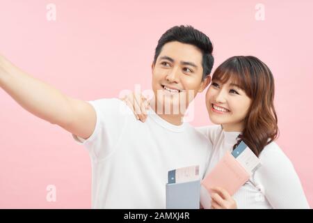 joyeux homme et femme d'asie qui détiennent des passeports et des billets d'avion tout en regardant la caméra isolée sur le rose Banque D'Images