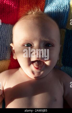 Un bébé riant heureux posé sur une couverture tricotée brillante Banque D'Images
