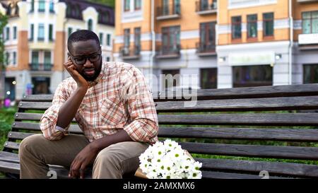 Bouleversé l'homme afro-américain assis seul sur un banc de ville avec bouquet, date de faillite Banque D'Images