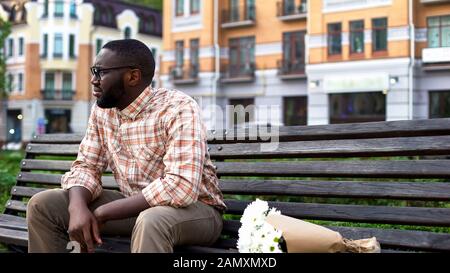 Triste homme africain assis seul sur un banc de ville avec bouquet de fleurs, date d'échec Banque D'Images