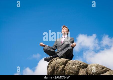 Businessman assis dans une pose de yoga en plein air en équilibre sur le haut de rocky mountain peak Banque D'Images