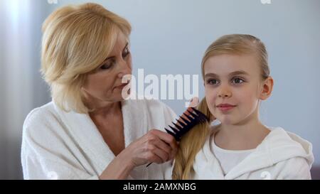 Grand-mère bienveillante peignant les cheveux de petite-fille devant le miroir, l'amour de famille Banque D'Images