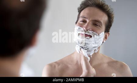Un homme heureux et confiant mettant la crème de rasage sur son visage avant de se raser Banque D'Images