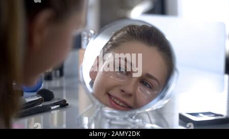 Femme avec des taches de gel sous les yeux regardant dans le miroir et sourire, soins anti-âge Banque D'Images