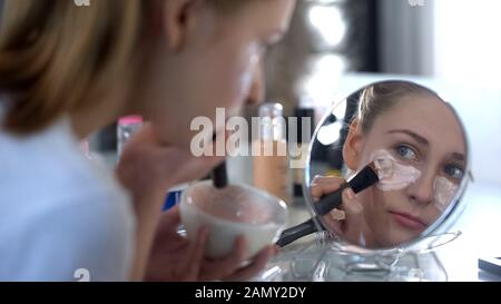 Jolie jeune femme mettant soigneusement masque d'alginate hyaluronique sous les yeux, beauté Banque D'Images