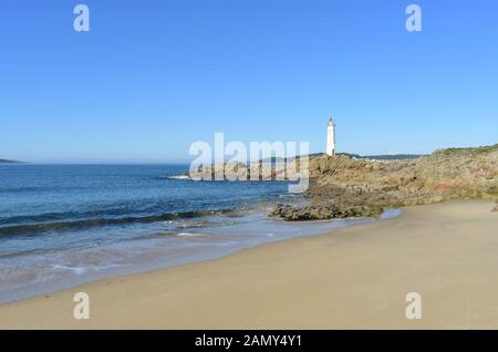 Plage avec sable humide, rochers et phare avec ciel bleu. Muxia, Galice, Espagne. Banque D'Images