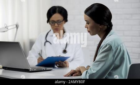 Médecin de la femme qui tient les dossiers médicaux attentivement à l'écoute des symptômes du patient Banque D'Images