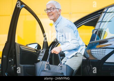 Senior businesswoman avec sac à sortir de sa voiture. Femme mature sophistiqués de descendre la voiture. Banque D'Images