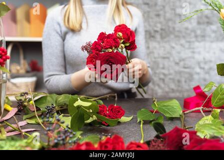 Une belle fille recueille un bouquet de roses rouges de bourgogne dans son studio. Male florist création magnifique bouquet dans le magasin de fleurs. Livraison de fleurs Banque D'Images