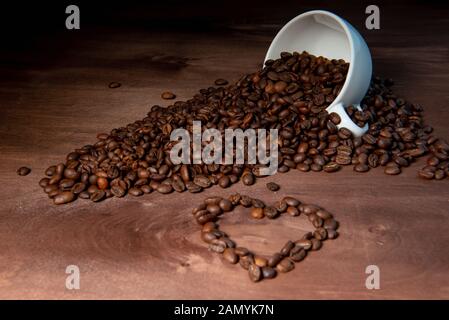 Le cafe du versant d'un mug blanc sur une table en bois, forme de coeur à partir de grains de café dans l'avant-plan - image Banque D'Images
