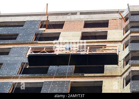 Construction suspendu berceau près de mur de hightower residentaial avec isolation du bâtiment et façade ventilée sur chantier de construction. Engineering Banque D'Images