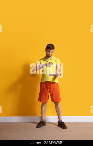 Choqué, s'est demandé. Jeune homme caucasien utilisant smartphone, serfing, chat, Paris. Portrait complet isolé sur fond jaune. Concept des technologies modernes, des millénaires, des médias sociaux. Banque D'Images