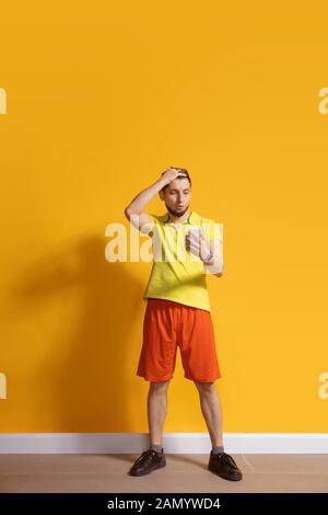 Choqué, s'est demandé. Jeune homme caucasien utilisant smartphone, serfing, chat, Paris. Portrait complet isolé sur fond jaune. Concept des technologies modernes, des millénaires, des médias sociaux. Banque D'Images