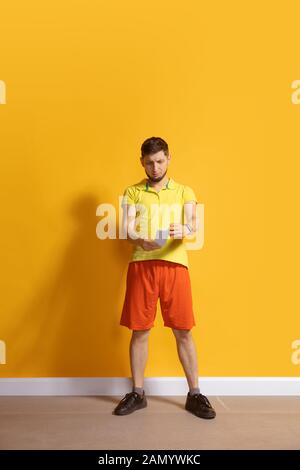 Choqué, s'est demandé. Jeune homme caucasien utilisant smartphone, serfing, chat, Paris. Portrait complet isolé sur fond jaune. Concept des technologies modernes, des millénaires, des médias sociaux. Banque D'Images