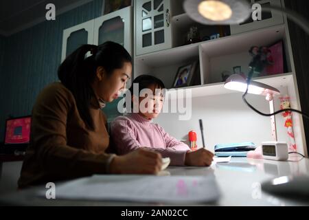 (200115) -- TAIYUAN, le 15 janvier 2020 (Xinhua) -- Chen Haiyan (L) aide sa fille à faire ses devoirs à domicile à Taiyuan, dans la province de Shanxi en Chine du nord, le 14 janvier 2020. Alors que des millions de Chinois renouent avec le festival de la veille du printemps, le nouvel an lunaire de la Chine, Zhao Yao et Chen Haiyan, un couple travaillant tous deux comme chefs d'orchestre sur les trains, rateront à nouveau l'anniversaire de leur fille qui tombe le même jour de la veille, Aussi l'occasion la plus importante de réunion de famille pour les Chinois. Il n'y a que trois fois que le couple passe l'anniversaire avec sa fille depuis qu'elle est née en 2008. Banque D'Images