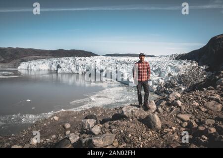 Un jeune homme traveler'debout devant Eqip Sermia appelé glacier Eqi Glacier. Mur de glace en arrière-plan. La notion de réchauffement global et Banque D'Images