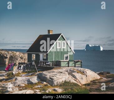 Maison typique de pêcheurs en bois coloré avec iceberg à Qeqertarsuaq, baie de Disko Groenland et Ilulissat. Architecture typique dans le cercle arctique. Banque D'Images