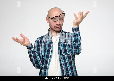 Homme chauve et stupide avec une grimace sur le visage, portant des lunettes de slanting et faisant un geste étrange avec les mains. Banque D'Images