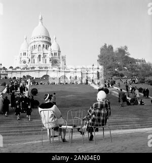 Années 1950, historiques, deux dames en parisien manteaux et chapeaux assis sur des chaises sur l'herbe ci-dessous les étapes menant à la célèbre monument, l'église catholique romaine en dôme, Sacré-Cœur, qui se repose sur une crête montagneuse à Montmartre, Paris, France. Banque D'Images