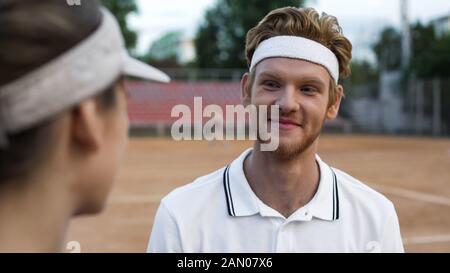 Sourire joueur de tennis masculin flirtant avec belle dame au court, passe-temps actif Banque D'Images