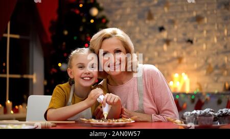 Femme retraité et petite-fille décorant les biscuits de Noël souriant dans l'appareil photo Banque D'Images