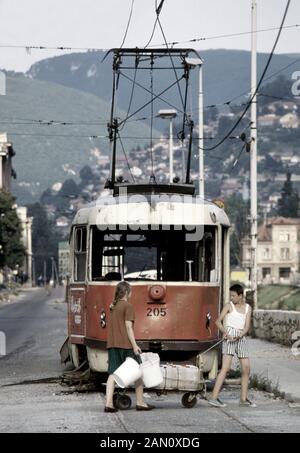 17 août 1993 Au cours du siège de Sarajevo : lors d'un cessez-le-feu temporaire, une jeune fille porte des seaux vides et un jeune garçon tire un chariot chargé de conteneurs en plastique remplis d'eau, après un tramway naufragé sur Obala Kulina Bana (anciennement appelé Obala Vojvode Stepe). Banque D'Images