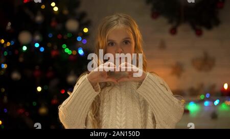 Enfant faisant du coeur avec les mains regardant l'appareil photo, l'amour et la charité à Noël Banque D'Images