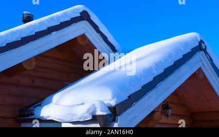 Transport de la neige sur le toit, d'après des chutes de neige sur la journée ensoleillée. Maison en bois dans la neige. Banque D'Images