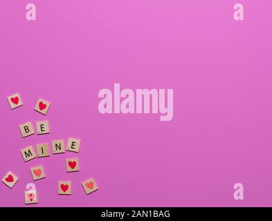 Be Mine valentine colorés tuiles jeu avec des cœurs dans le coin d'un fond rose Banque D'Images