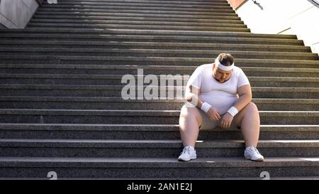 Homme gras assis sur les escaliers après le jogging, pas de foi en lui-même, insécurités Banque D'Images