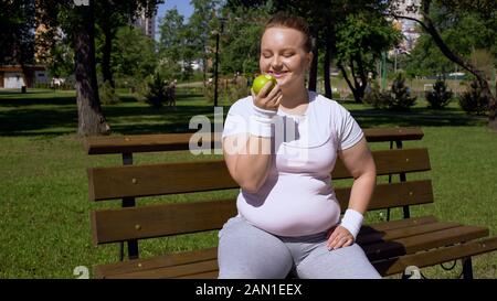 Une fille obèse mangeant la pomme après le jogging, un régime sain, un déjeuner approprié avec des vitamines Banque D'Images