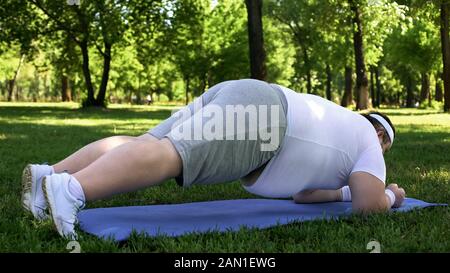 Homme obèse faisant planche dans le parc, programme de perte de poids, forte volonté, motivation Banque D'Images