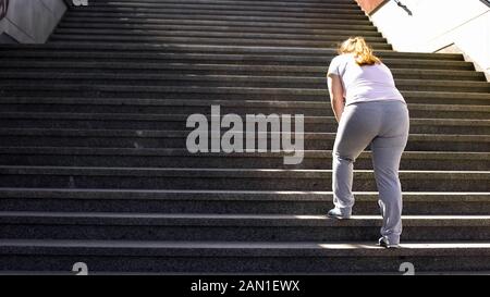 Difficile de monter des escaliers pour une fille obèse, victoire sur la fatigue pour atteindre le but Banque D'Images