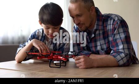 Curieux père et petit fils examinant le nouveau modèle quadrocopter à la maison, amusant Banque D'Images