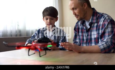 Un petit garçon excité exploitant un nouveau modèle de drone à la maison, père aidant son fils Banque D'Images