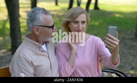 Jolie femme âgée à l'appareil photo de votre smartphone en réflexion, en tenant selfies Banque D'Images