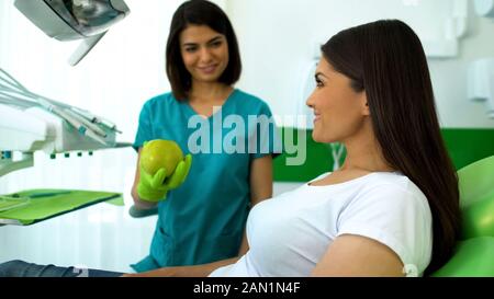 Dame souriante dentiste pomme verte donnant au patient, les soins de recommandations Banque D'Images
