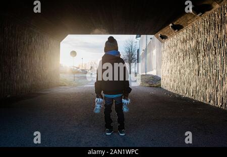 jeune garçon debout dans un tunnel tenant ses patins à glace en hiver Banque D'Images