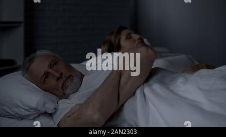 Agacé Senior homme étendu dans le lit se tourna vers la femme, l'incompréhension, querelle Banque D'Images
