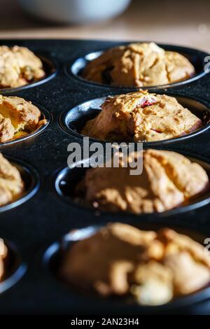 Gros plan sur une rangée de délicieux muffins cerise vanille vegan dans un moule à muffins noir dans la lumière du soleil du matin - vue oblique verticale, orientation portrait Banque D'Images