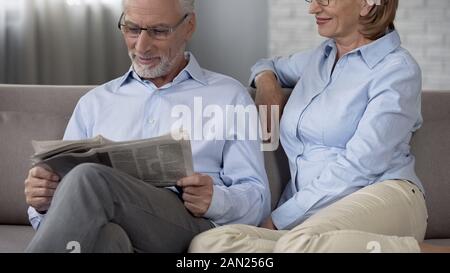 Senior male lire le journal du matin, dame serrant tendrement son mari, l'amour Banque D'Images